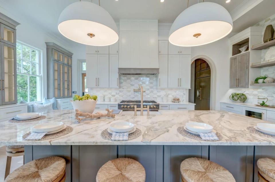 Kitchen with a marble island, two large white pendants and a gold faucet